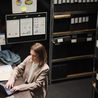 Aerial-view of detective arranging files and evidence, preparing to leave the office. After completing research on criminal case investigation, female investigator closes her laptop on workstation.