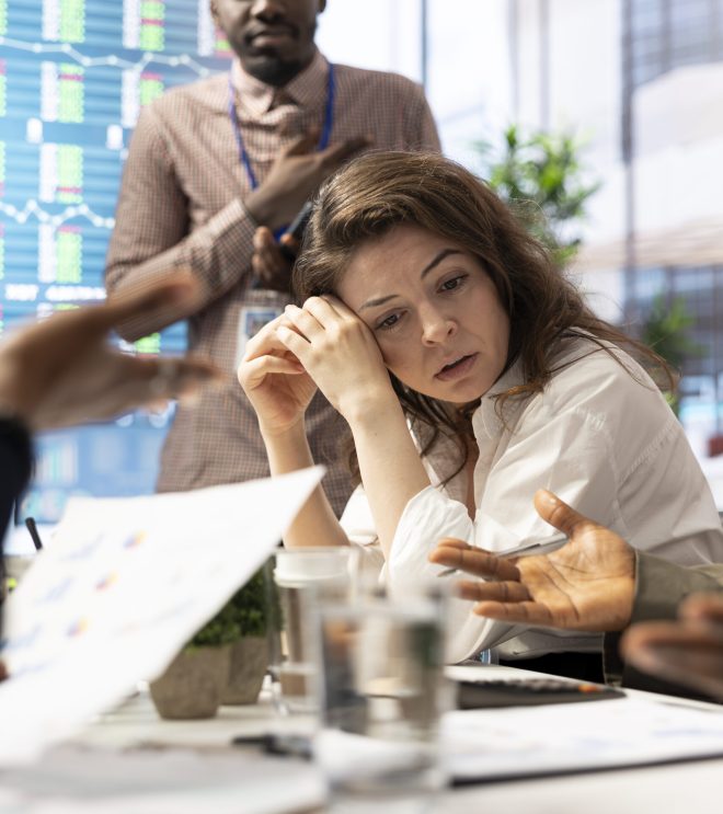 Female general manager trying to handle the organizational crisis during a meeting with staff, feeling exasperated and dissatisfied with progress and efficiency. Frustrated employee under pressure.