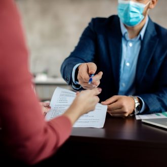 Close-up of a insurance agent closing a deal with a client in the office during coronavirus pandemic.